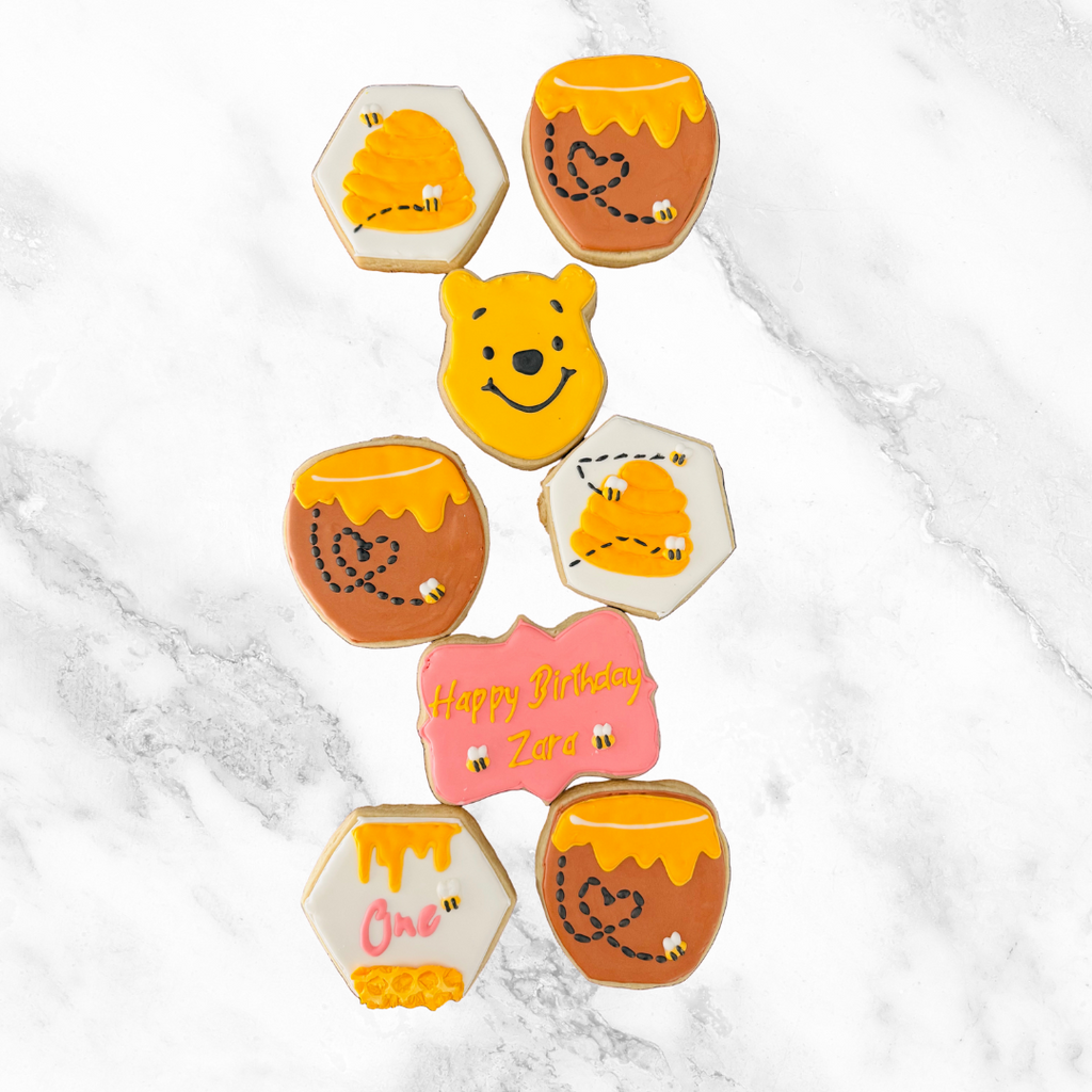 Decorative cookies shaped like Winnie the Pooh and honeycomb on a marble surface
